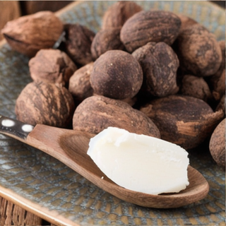 Ein Stück Sheabutter auf einem Löffel mit Sheanüssen im Hintergrund