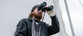 Mann mit Bart schaut durch Fernglas auf einem Segelboot